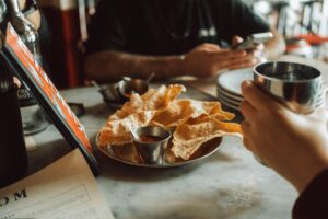 Crispy papad served with chutney at a casual dining setting with people enjoying drinks.