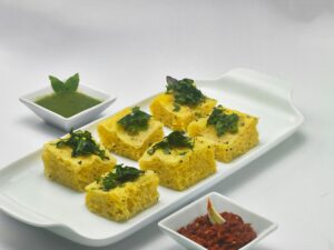 A vibrant serving of traditional Indian dhokla with two types of chutney on a white platter.